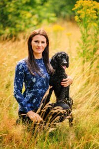 A woman and her black poodle share a serene moment, seated in the midst of a wildflower meadow in Nottingham.
