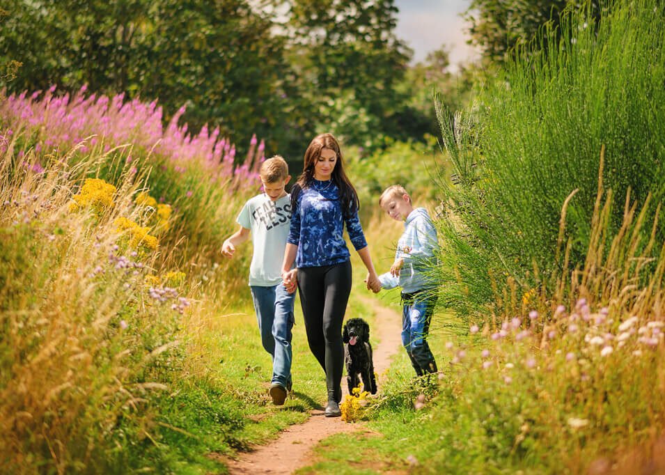 A leisurely walk through Nottingham's vibrant countryside, as a woman and two boys enjoy the company of their black poodle among the wildflowers.