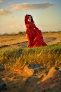 Elegant woman in flowing red dress posing gracefully in a golden field during sunset for an outdoor birthday photoshoot.