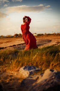 A woman in a vibrant red dress strikes a captivating pose against a serene landscape during an outdoor birthday photoshoot.