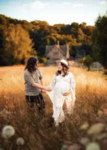 Maternity photographer in Nottingham captures couple holding hands in golden field.