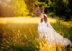 Pregnant woman in lace dress smiling joyfully in a Nottingham field at sunset.