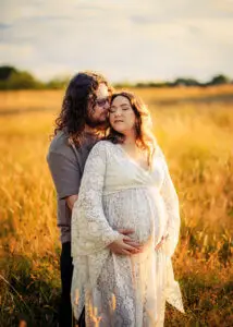 Couple in Nottingham field with pregnant woman cradling her belly during sunset.