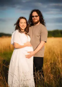 Expectant couple in a Nottingham field at sunset, maternity photographer captures a vibrant scene.