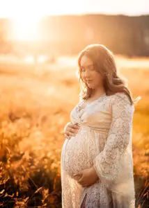 Pregnant woman caressing her belly in the glowing light of sunset, photographed in Nottingham.
