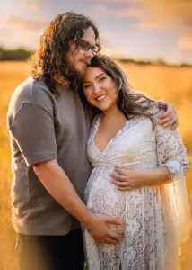 Maternity photographer Nottingham captures a couple's tender embrace at sunset in a field.