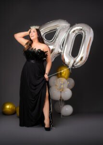 Woman wearing a crown and black dress, laughing with '40' balloons in her 40th birthday photoshoot.