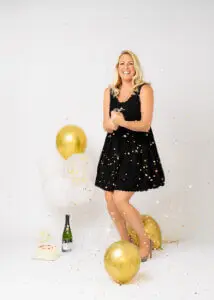 Blonde woman in black dress celebrating her 40th birthday photoshoot with confetti and gold balloons.
