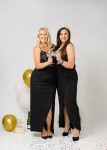 Two women in black dresses, wearing crowns and toasting with crystal glasses during a 40th birthday photoshoot.