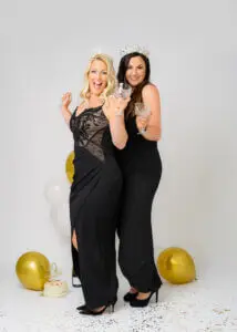 Two women in black dresses and crowns, celebrating with crystal glasses during a 40th birthday photoshoot.