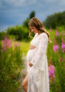 Pregnant mother in a white lace gown holding her belly in a wildflower field during a maternity photo shoot in Nottingham