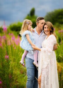 Expecting father kissing his pregnant wife with daughter in a wildflower field during a maternity photo shoot in Nottingham