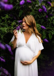 Pregnant mother in white dress admiring flowers in a garden during a maternity photo shoot in Nottingham