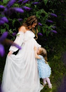 Pregnant mother with her daughter in a garden, surrounded by purple flowers during a maternity photo shoot in Nottingham