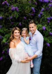 Happy pregnant mother with her family in front of purple flowers during a maternity photo shoot in Nottingham