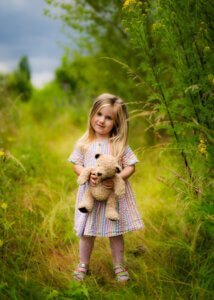 Little girl holding a teddy bear in a meadow during a maternity photo shoot in Nottingham