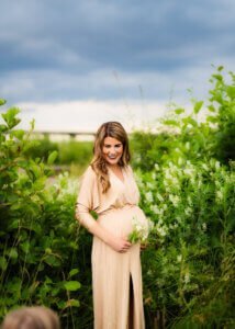 Pregnant mother in a golden dress standing in a green meadow during a maternity photo shoot in Nottingham