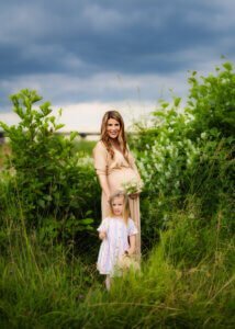 Pregnant mother and daughter standing together in a green meadow during a maternity photo shoot in Nottingham