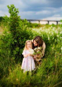 Pregnant mother and daughter picking flowers together in a meadow during a maternity photo shoot in Nottingham