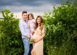 Happy family including pregnant mother, father, and daughter smiling in a green meadow during a maternity photo shoot in Nottingham