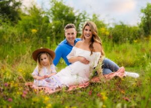 Expecting parents sitting on a blanket with their daughter in a wildflower meadow during a maternity photo shoot in Nottingham
