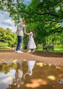 Engaged couple dancing joyfully with their reflection in a puddle during their Nottingham engagement photoshoot.