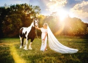 Woman with a long veil standing with her horse during a sunset equine photoshoot