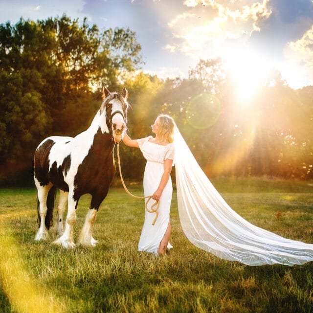 Woman with a long veil standing with her horse during a sunset equine photoshoot