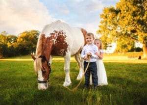 Children standing with a horse in a rural field during a family equine photoshoot