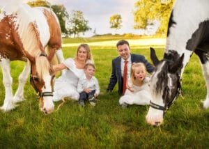 Family sitting in a field with two horses during an outdoor equine photoshoot