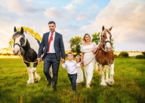 Family walking hand in hand with horses in a rural field during an equine photoshoot