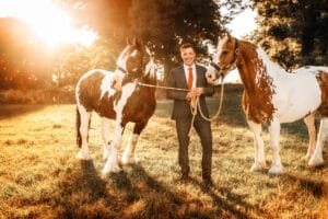 Man in a suit standing with two horses during a sunset equine photoshoot