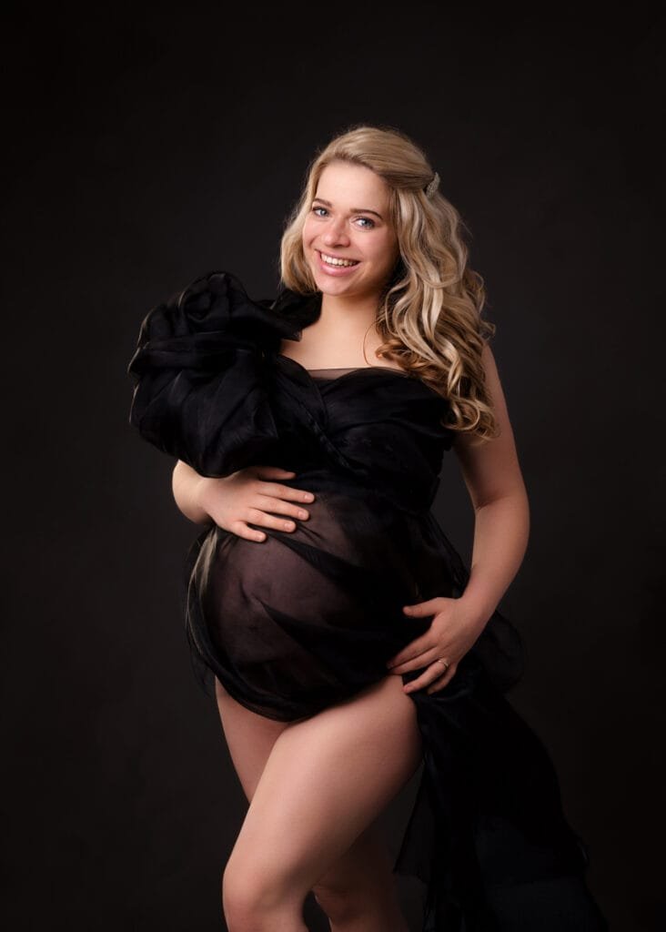 Radiant mom-to-be wearing a chic black maternity dress during her baby bump photoshoot in Nottingham studio.