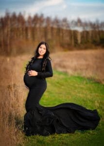 Pregnant woman posing in a black maternity photoshoot dress outdoors