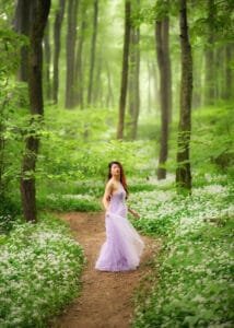 Elegant women portrait photography in Nottingham featuring a woman in a flowing lavender dress walking through a dreamy forest covered in wild garlic flowers