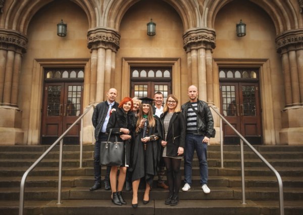 A graduate in academic regalia celebrating with family on the steps of a historic Nottingham university building.