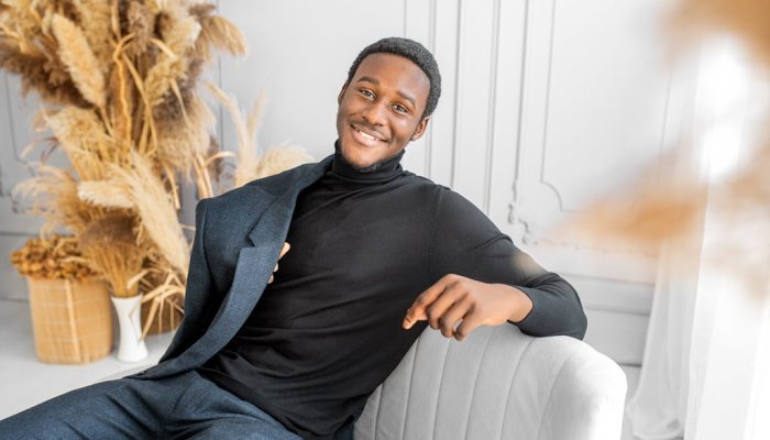 Modern men’s photoshoot featuring a stylish man in a black turtleneck and suit, relaxed and smiling.