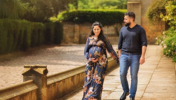 A couple walks hand-in-hand in a serene garden, the pregnant mother's floral gown capturing the essence of growth and new beginnings in their maternity photography.